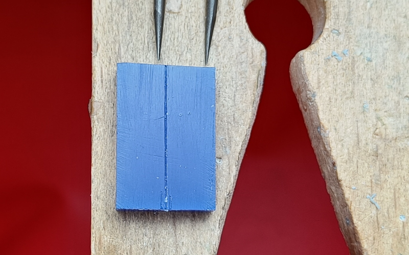 Close up of piece of blue wax with 2 small lines marked on it and one long line marked through the middle