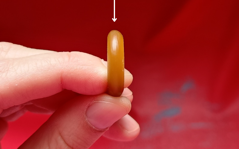 Close up of hands holding a piece of gold ring wax. An arrow is pointing to the back on the ring where you should look at