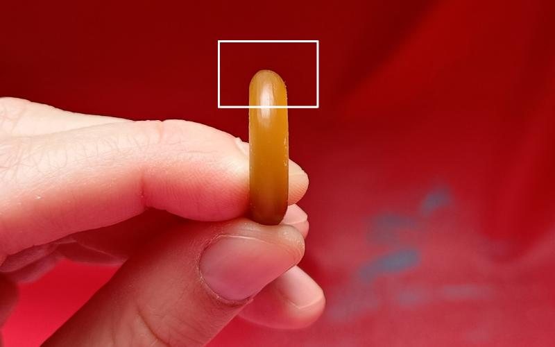 Close up of hands holding a piece of gold ring wax. A rectangle is drawn around the back section on the ring where you should look at
