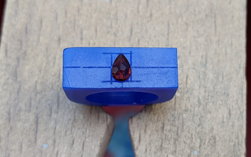 blue ring wax blank on bench peg with lines drawn on and a solitaire garnet in the centre