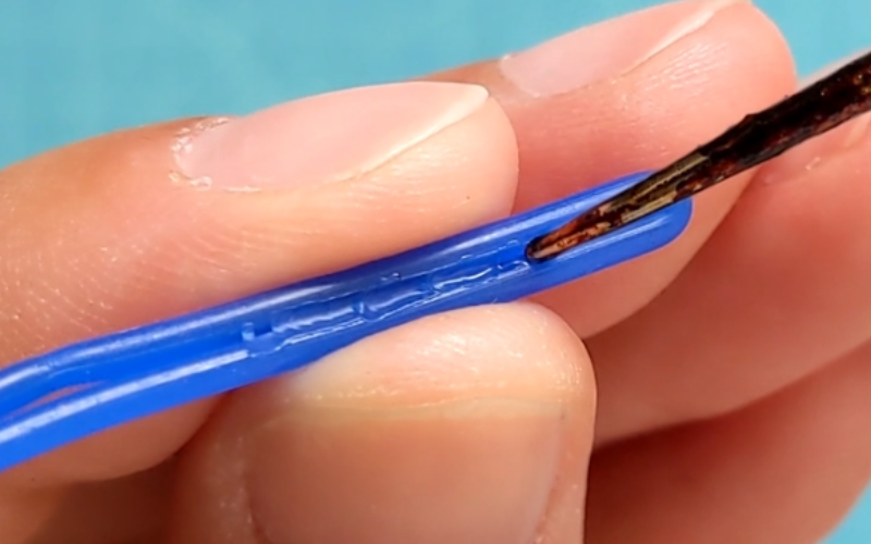 Close up of hands holding a piece of doubled blue wax wire. Wire is being melted together with a wax heating pen