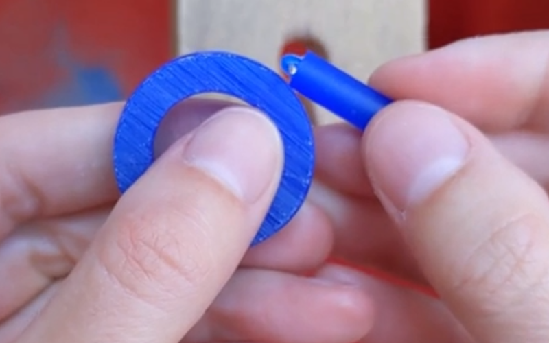 close up of hands holding a donut shape blue wax piece and a rectangular blue wax piece. The pieces are held together, trying to figure out how they can move