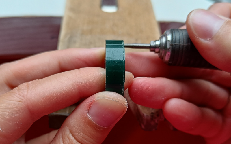 Close up of a hands holding a piece of ring wax and burr. The burr is behind the ring wax and you can't see it 