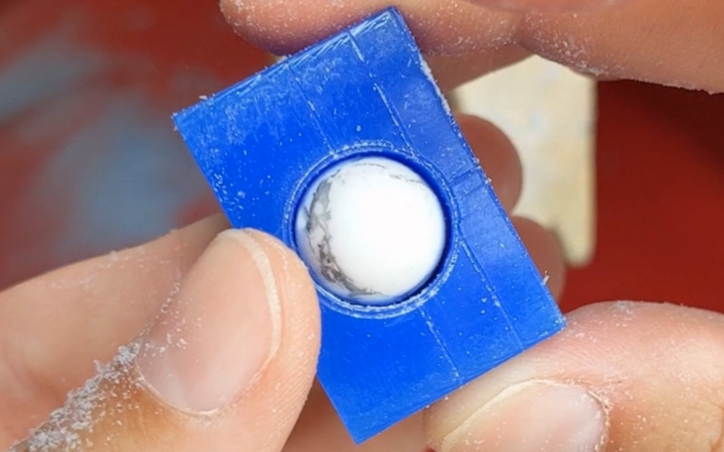  Close up of hands holding a piece of blue ring wax. A hole has been made in the centre of the ring and a bead is placed in the hole