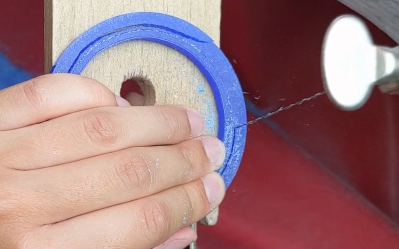 Close up of hands piercing away wax from the outside of a blue wax bangle