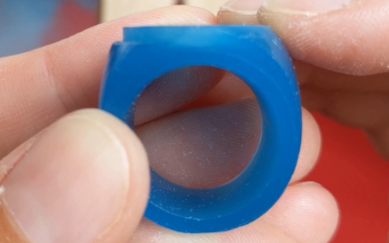 Close up of hands holding a turquoise wax ring that's still in progress. One the left side the setting wall is becoming visible.