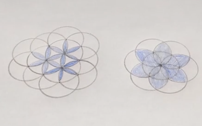 Piece of paper with flower patterns drawn on it with a compass. Parts of the pattern are colored blue