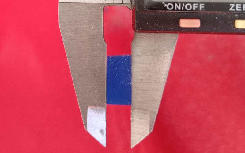 Close up of a piece of wax in the jaws of the calipers. Towards the top of the piece of wax, light is coming through between the wax and the jaws.