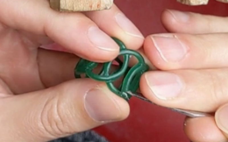 Hands carving the shape in an overlapping ring from green wax 