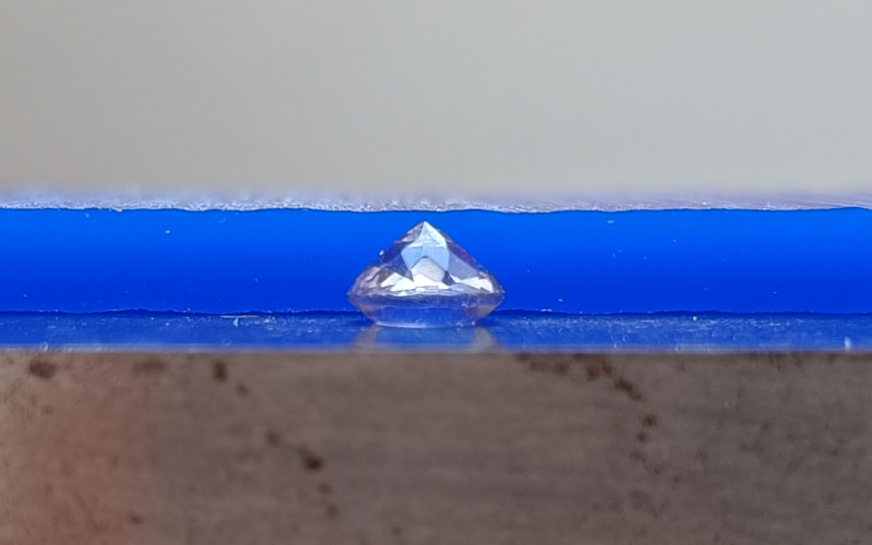 Close up of gemstone lying on top of a steel block with a piece of wax behind it that is a small bit thicker than the gemstone