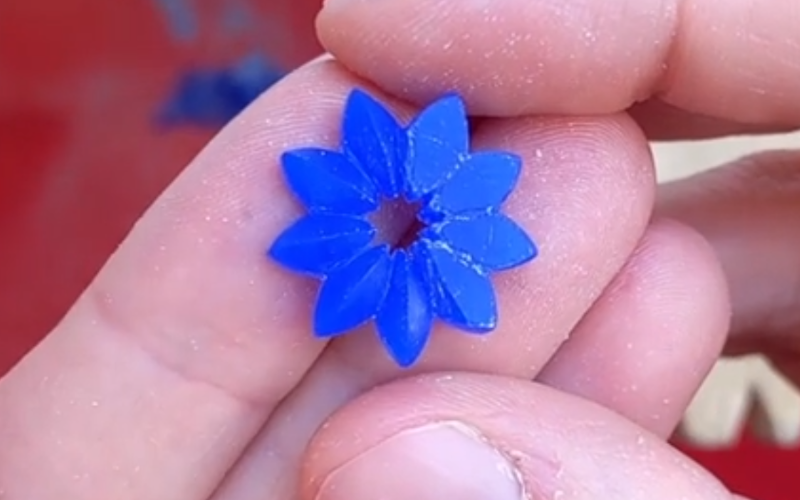 Close up of hands holding a blue wax flower in process. The left half of the petals are shaped the right side is still rough