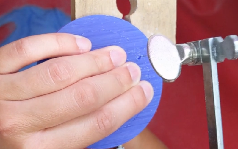 Close up of hands piercing a slice of blue wax, you can see the drill hole is close to where the hands are piercing 