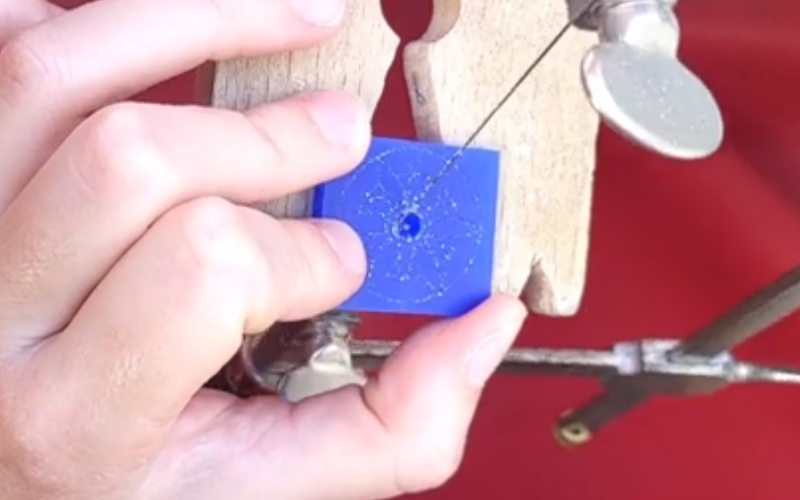 close up of hands working at the bench. The left hand is holding a piece of blue wax and the right hand is piercing a section in the middle of it.