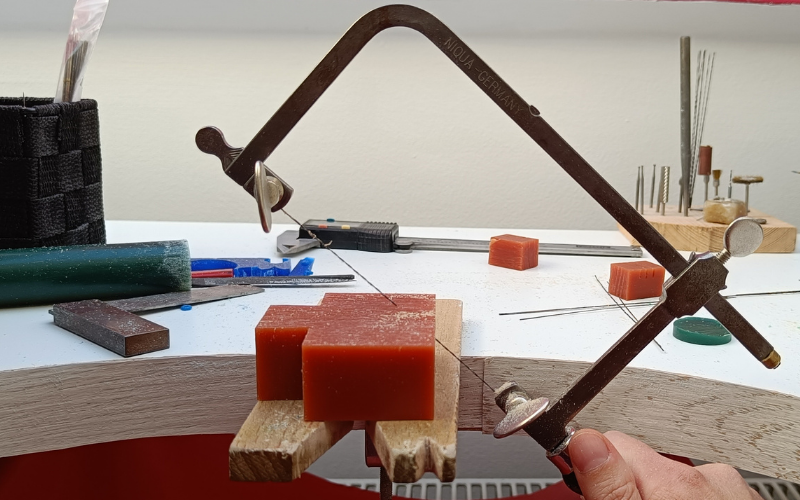 orange block of wax and a hand holding a saw at an angle piercing the wax