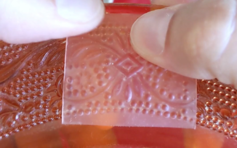 CLose up of hands pushing a piece of pink sheet wax on a textured plate