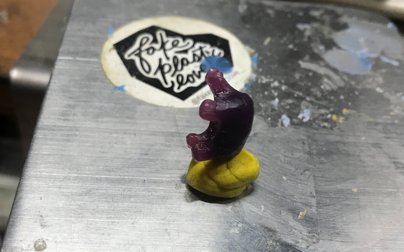 Close up of bench with a piece of yellow playdough holding up a piece of purple wax