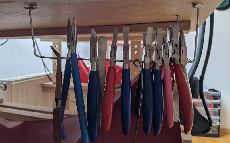 Wire shaped and attached to the bottom of the bench for plier storage