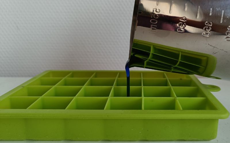 close up of pouring liquid blue wax into the ice cube mould