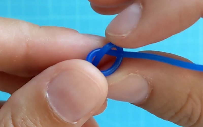 Close up of hands holding a knotted piece of blue wax wire, Fingers are pushing on the knot to make it tighter