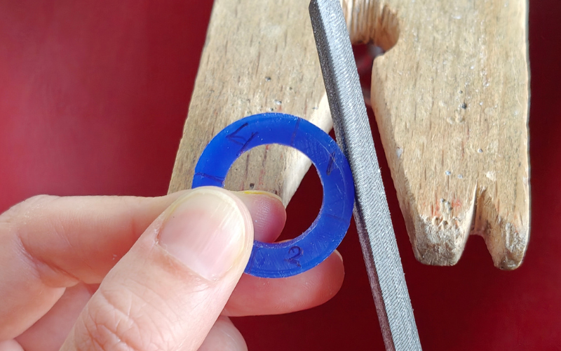 Close up of hands holding a blue wax ring, left thumb holding the ring is covering section 3, the file is against section 1
