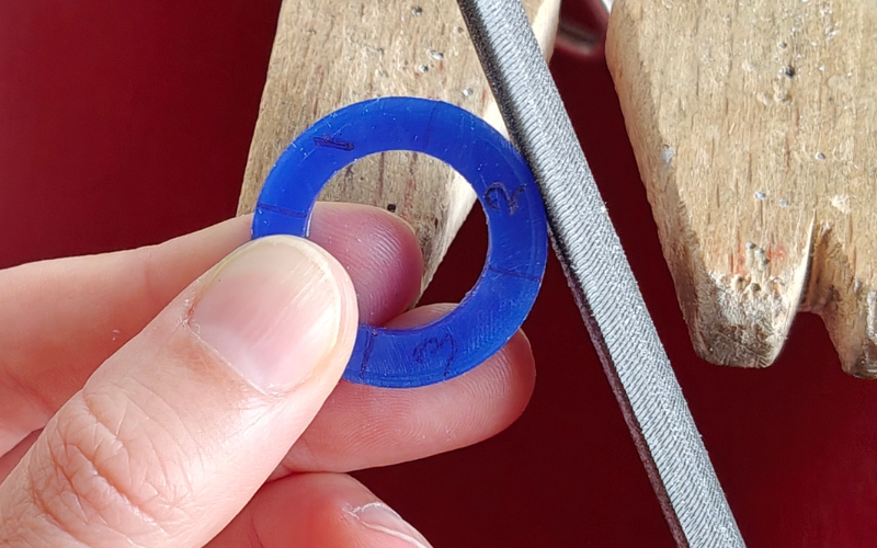 Close up of hands holding a blue wax ring, left thumb holding the ring is covering section 4, the file is against section 2