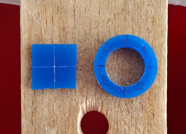 Close up of 2 pieces of blue wax on a bench peg. Left a square with center lines marked on top, right a ring divided in 4 with marker and numbers from 1-4 written in each section