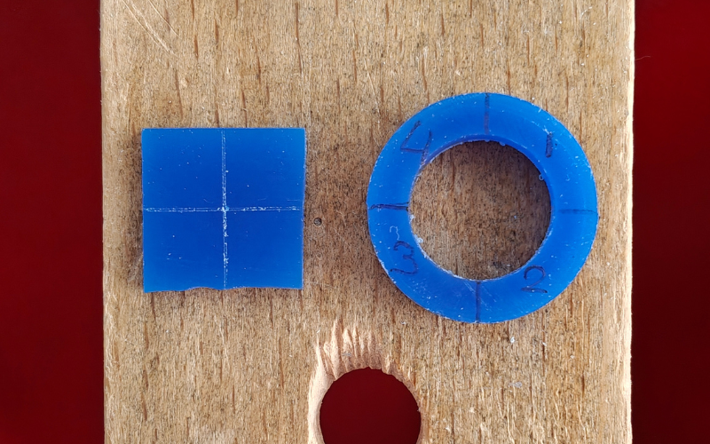 Close up of 2 pieces of blue wax on a bench peg. Left a square with center lines marked on top, right a ring divided in 4 with marker and numbers from 1-4 written in each section