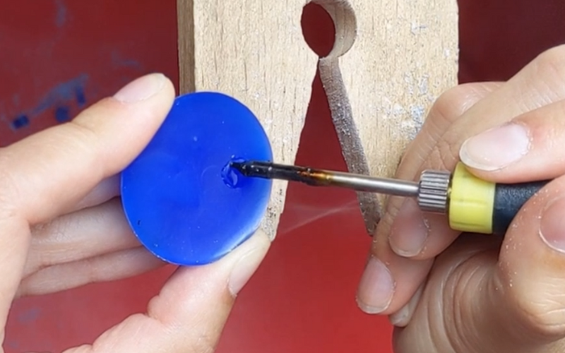  Close up of hands working at the bench. A small section of blue wax is being melted with a wax heating pen 