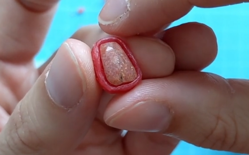Close up of hands holding a red wax bezel with a sunstone inside