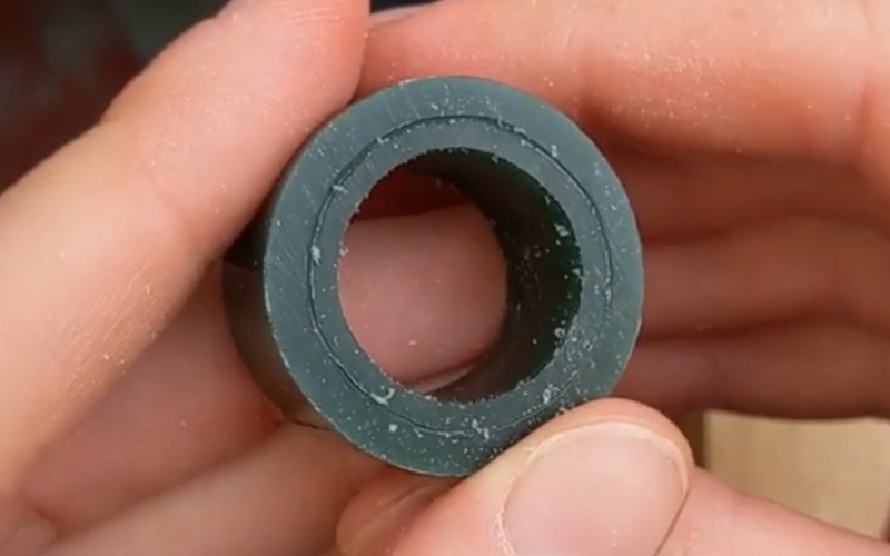 CLose up of hands holding an unfinished green wax ring blank. There is a mark on the side showing the depth it's going to be.