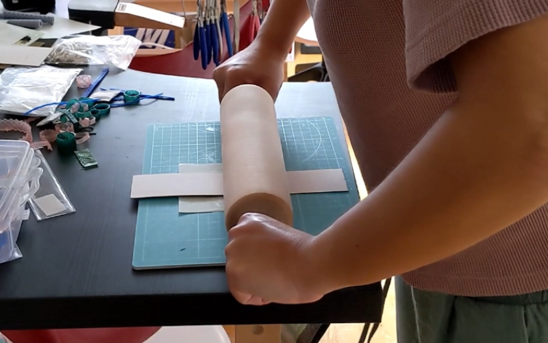 Close up of hands holdiong a rolling pin and rolling it over texture paper and sheet wax
