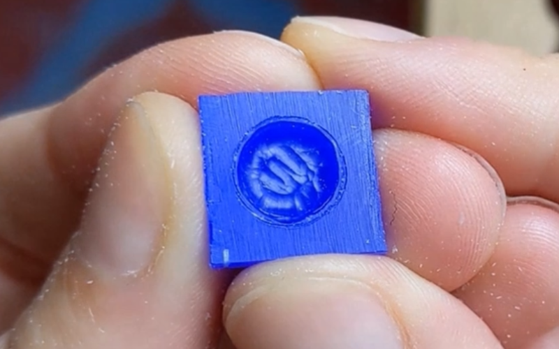 Close up of hands holding a piece of blue wax with a round opening carved away. the walls on the inside of the opening are curving in towards the bottom
