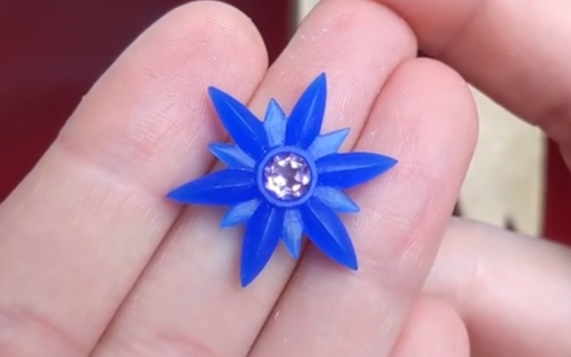 close up of hands holding a finished flower shape from blue wax with a purle round stone in the middle. 