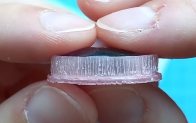 Close up opf hands holding a bezel from pink sheet wax showing the side profile. The setting wall has been textured with lines