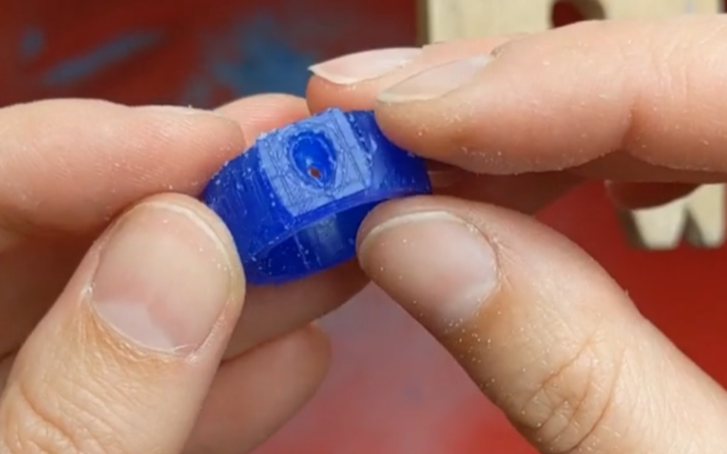 Close up of hands holding a blue wax ring with a seat cut out for a pear shaped stone. Parts of the ring band are cut down and it's looking pretty rough at the moment