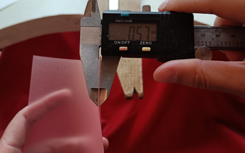 close up of hands measuring the thickness of a sheet of pink wax. The callipers read .57mm