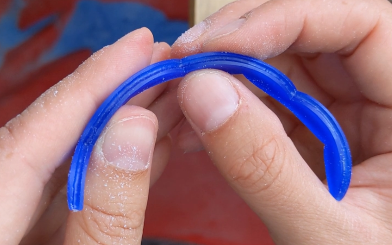 Close up of hands holding a blue wax bangle. You can see a line burred on the side. 