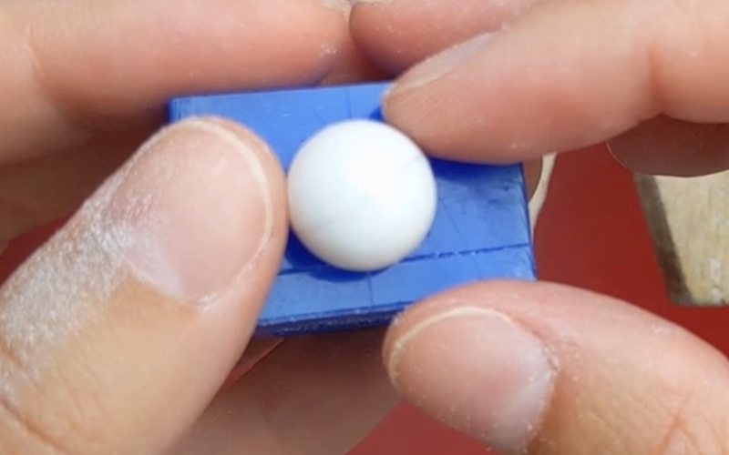  Close up of hands holding a piece of blue ring wax with a bead balancing on top