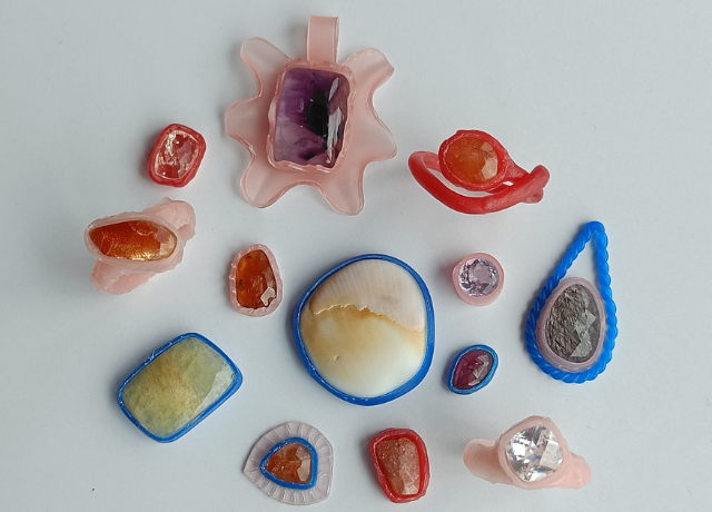 a mix of pendants and rings with all kinds of different color gemstones made from blue wax wire, pink sheet wax, and red mold-a-wax