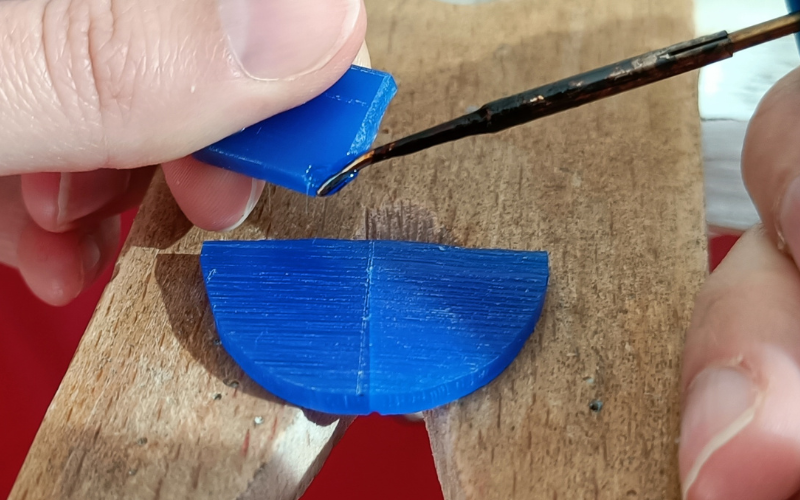 pieces of blue wax lying on bench peg. Hands holding s separate piece of wax that's being melted with a wax heating pen