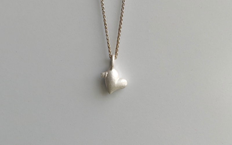 Zilveren hanger in een oneven hart vorm met gietkanaal links boven aan een zilveren ketting