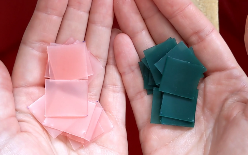 Close up of hands holding small square of green and pink sheet wax