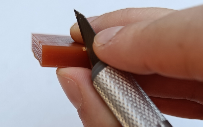 orange piece of wax with stanley knife in it and wax crumbling away from the cut