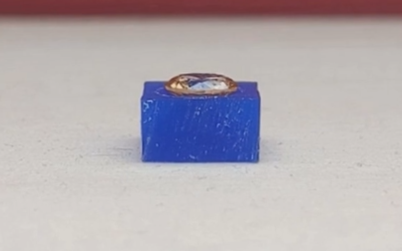 Close up of piece of blue wax with a yellow faceted stone inside. The girdle of the stone is still high over the wax