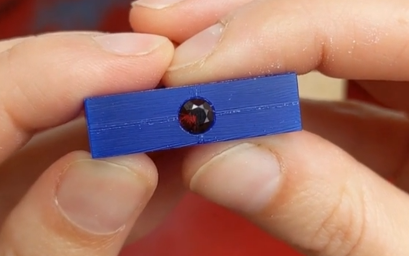 Close up of hands holding a blue wax ring with a seat cut out for a round stone.