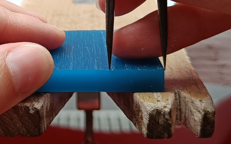 Hand holding a pair of dividers on the wax, the dividers are straight. 