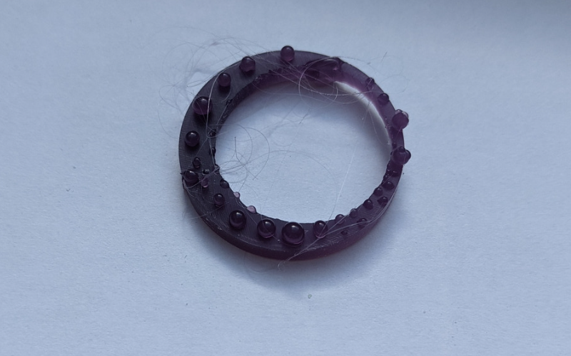 Close up of a purple wax ring with granulation and a lot of thin strings attached from using the heating pen