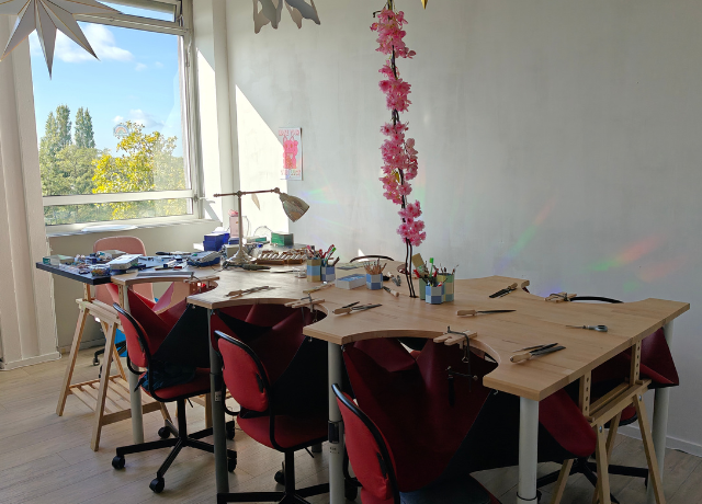 Studio space with big windows in the back, Big table with 6 jewellery benches is in the middle and 1 smaller jewellery bench at the end.