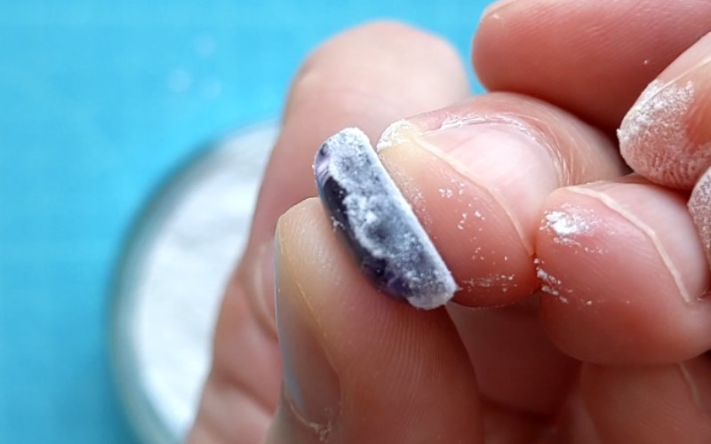 Close up of hands holding a cabochon purple stone that's just been dipped in talcum powder. You can see the posder on the side of the stone