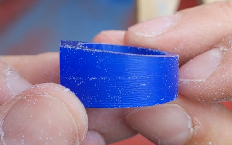 Close up of hands holding a blue wax ring. The top side of the ring is tapered, the bottom side is still flat.